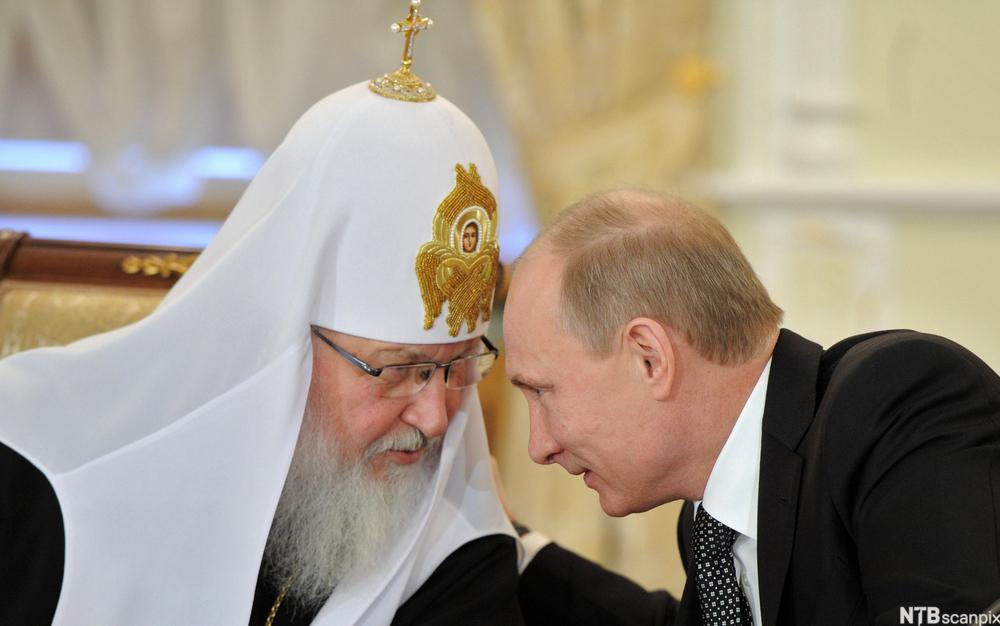 Mann med religiøst hodeplagg og stort skjegg lener seg mot og snakker med Russlands president Vladimir Putin. Foto.
