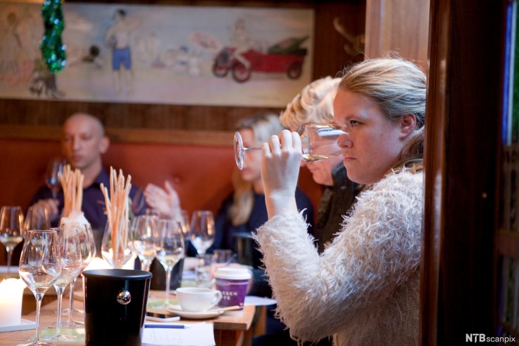 Mennesker rundt et bord smaker på vin. Foto.
