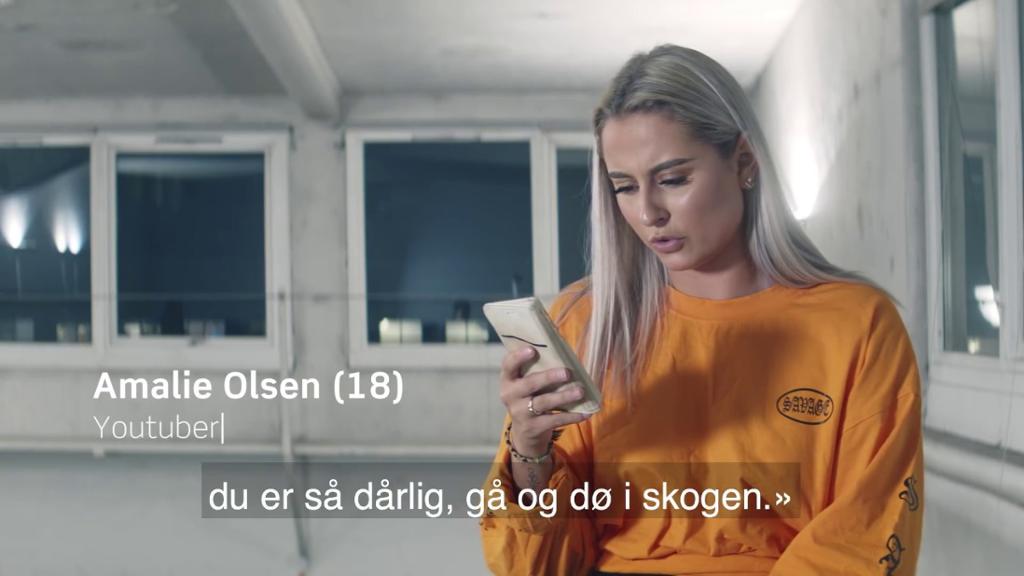 Jente som leser på mobilen. Det står at hun heter Amalie Olsen og er 18 år, og nederst står det "Du er så dårlig, gå og dø i skogen". Foto.