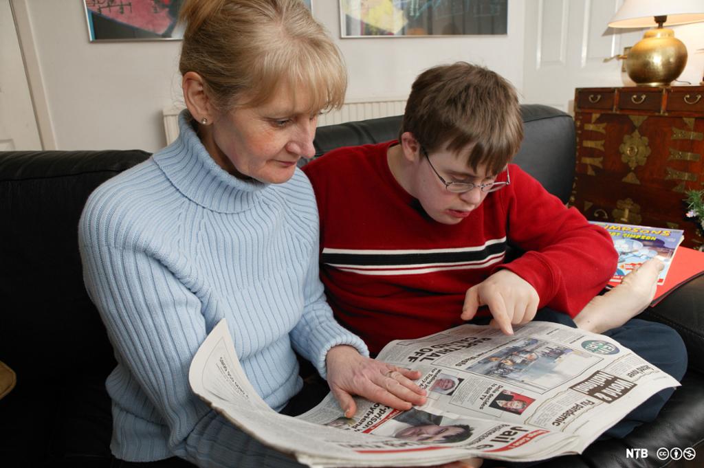 En gutt med Downs syndrom og en kvinne leser nyheter i en avis. Foto.