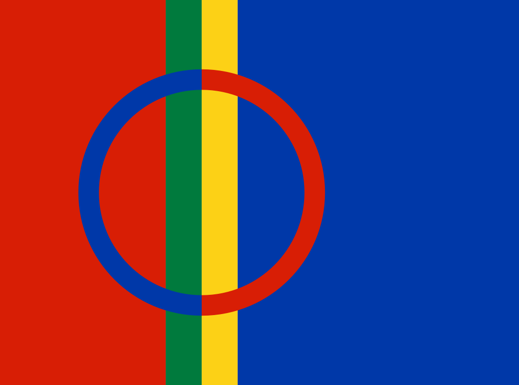 Flagg med fire vertikale fargebånd, rødt, grønt, gult og blått. En tofarget sirkel i blått og rødt overlapper fargebåndene. Foto.