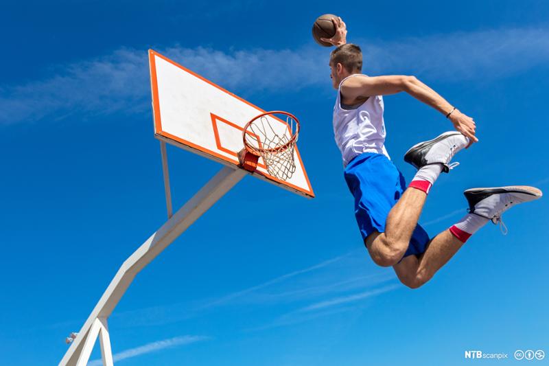 Basketballspiller hopper høyt og dunker en ball i kurven. Foto.
