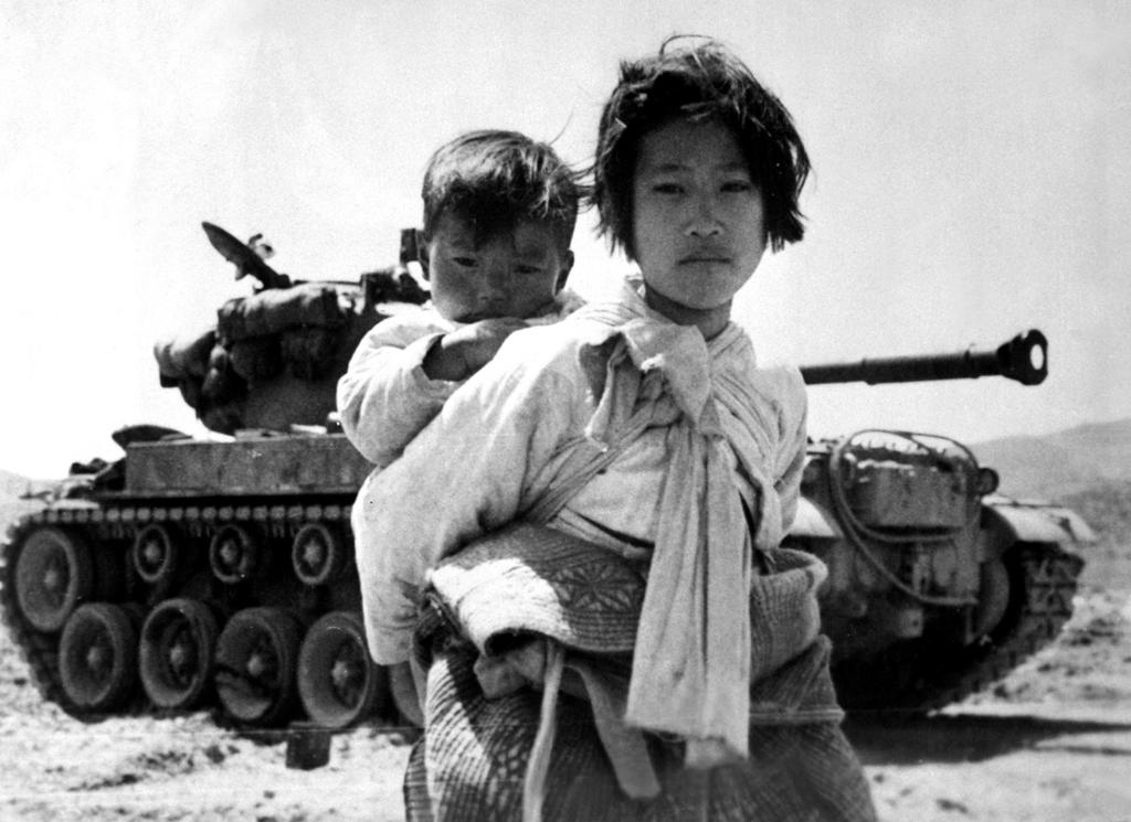 To koreanske barn foran ei stridsvogn. De er alvorlige og ser rett inn i kameraet. Svart-hvitt-foto.