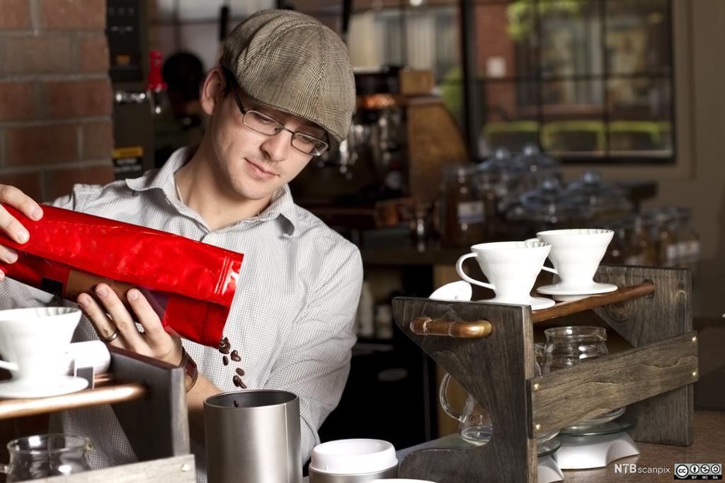 Person heller kaffebønner i en kaffekvern. Foto.