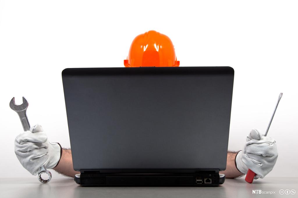 Person med hjelm og verktøy reparerer datamaskin. Foto.
