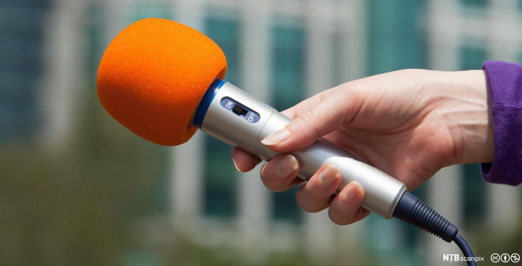 A hand holding an orange microphone. Photo.