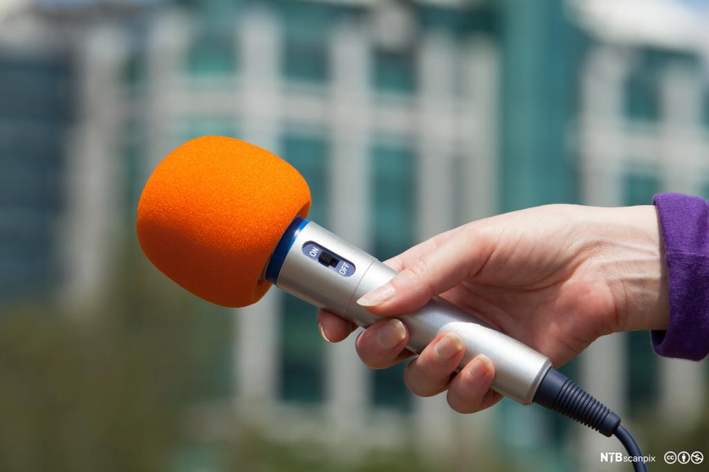 Nærbilde av kvinnehånd som holder en orange mikrofon. Foto.