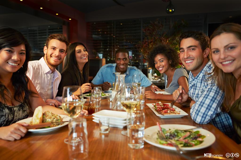 Smilende gjester rundt restaurantbord. Foto.