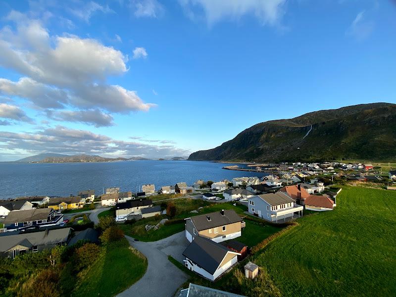 Photo: We see houses nestled by a fjord or a lake. There is a low mountain with a stream to the right. 