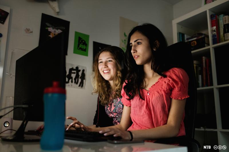 To jenter ser inn i en dataskjerm og smiler. Foto.