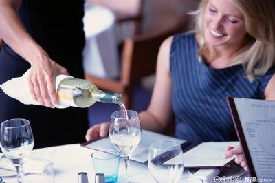 En servitør skjenker vin i glasset til en gjest. Foto.