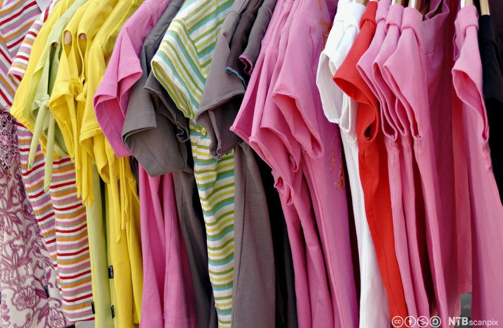 T-skjorter i ulike farger henger tett i tett på et stativ. Foto. 