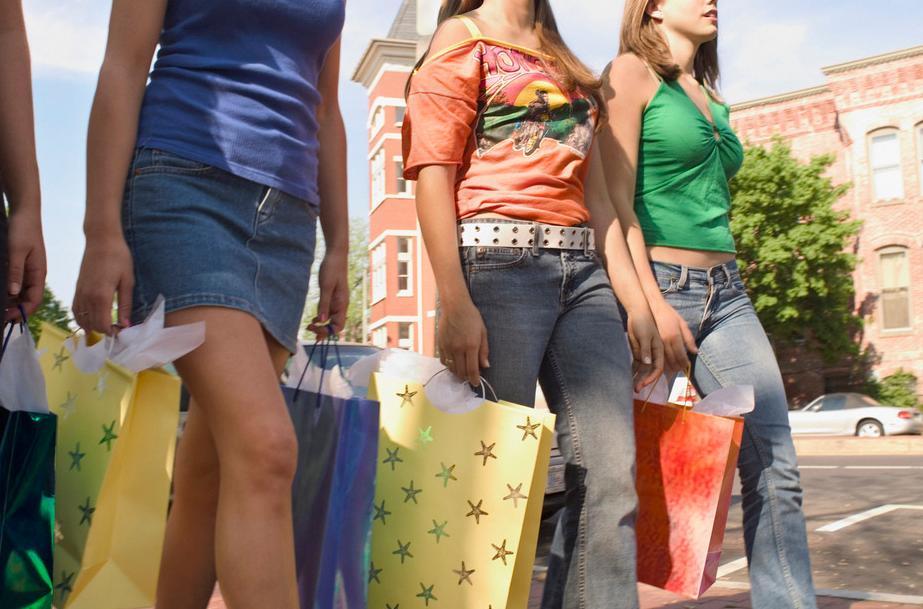 Fire tenåringsjenter i sommerklær går gjennom en gate med hver sine store, fargerike gaveposer. Foto.