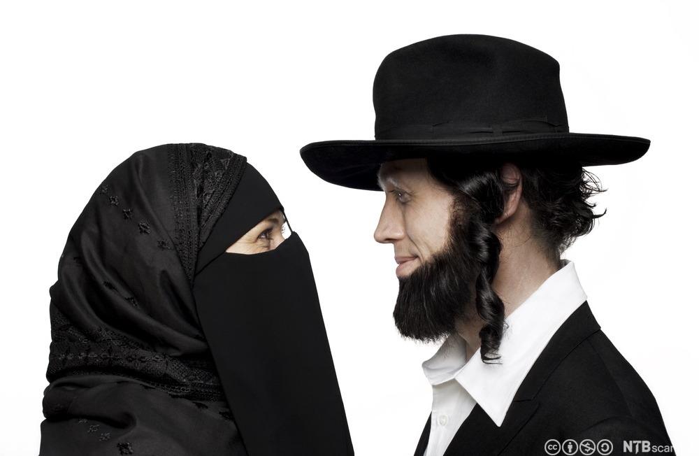 En kvinne tildekket med nikab og en mannlig konservativ jøde med hatt, skjegg og krøller som henger ned foran ørene. De to står ansikt til ansikt. Foto. 