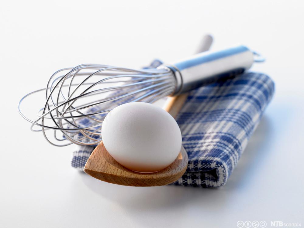 Et egg ligger på en tresleiv med en visp ved siden av. Foto.