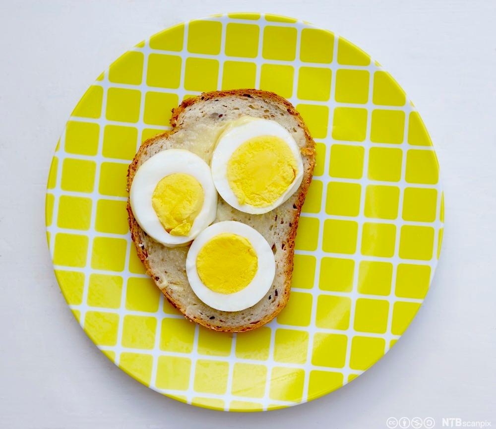 Brødskive med kokt egg på en gul asjett. Foto.