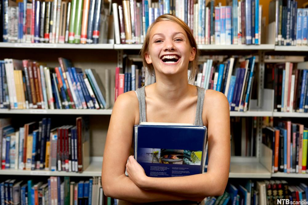 Smilende jente på bibliotek. Foto. 