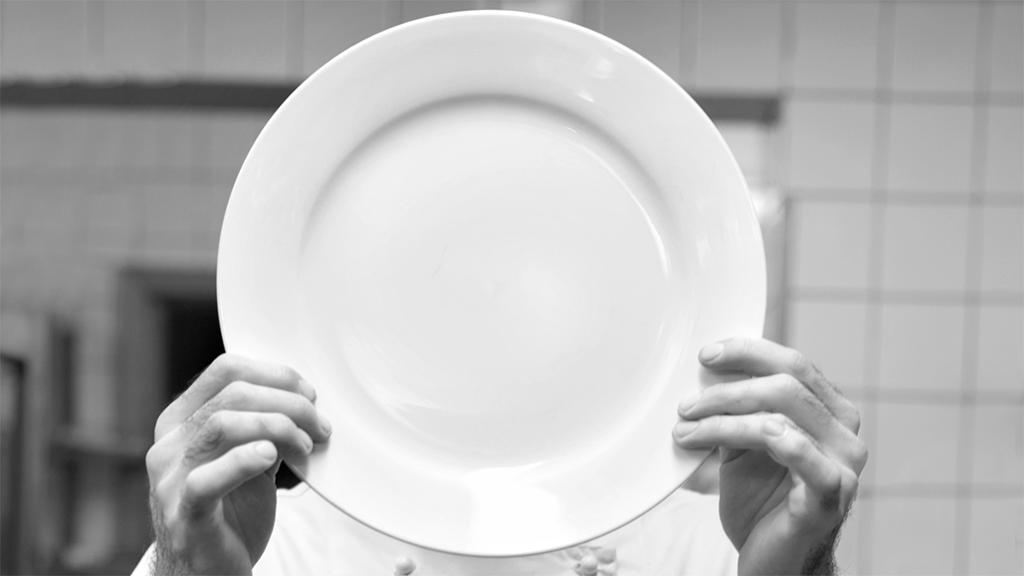 Kokk holder en tallerken foran ansiktet. Foto.