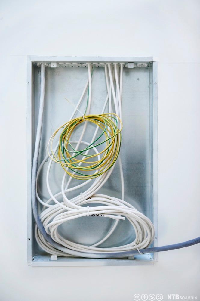 Åpent sikringsskap under installasjon med ledninger som henger ut. Foto.