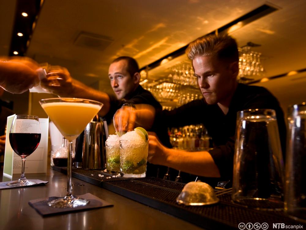 To mannlige bartendere lager drinker og tar imot betaling i en bar. Foto.