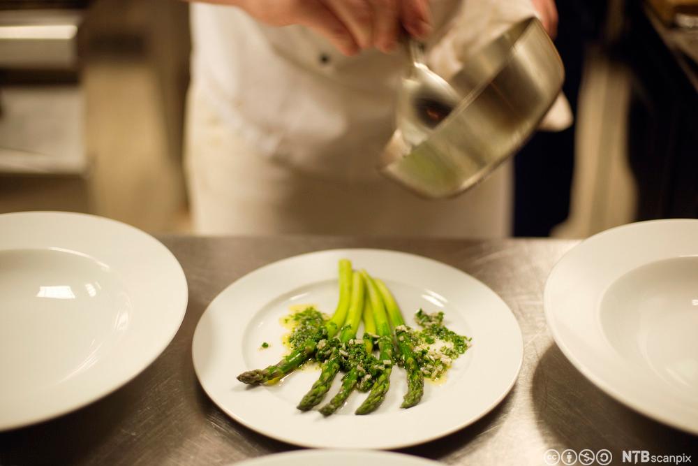 En kokk legger opp asparges på en tallerken. Foto.