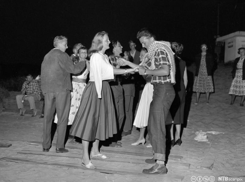 Ungdom kledd i 1950-talls mote danser utenfor et forsamlingshus for unge i 1957. Foto. 