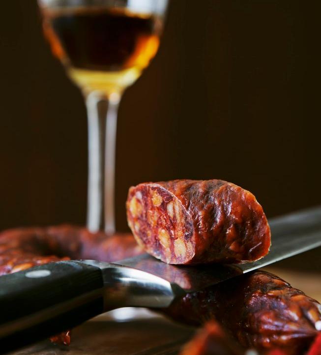 En chorizopølse, en kniv og et glass sherry. Foto.