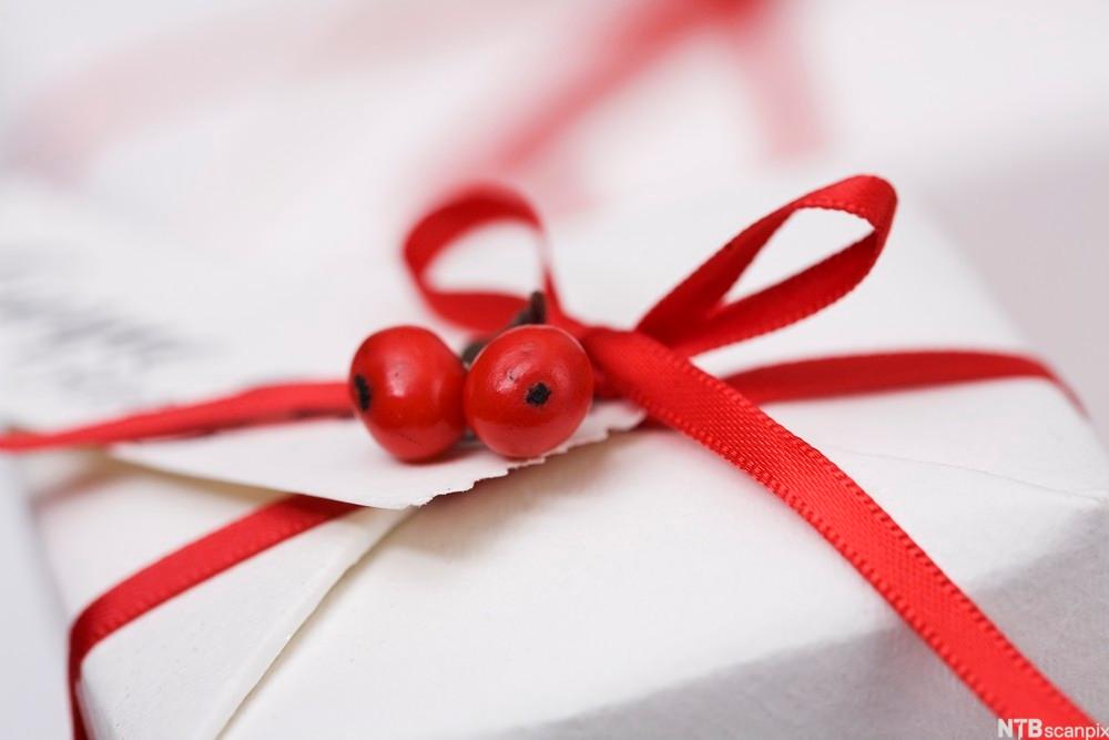 Photo: Gift wrapped in white paper with a red bow and two red berries. 