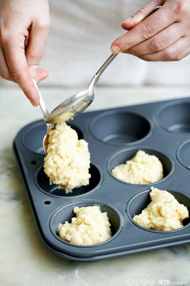 Setter klissete deig i muffinsformer. Foto.