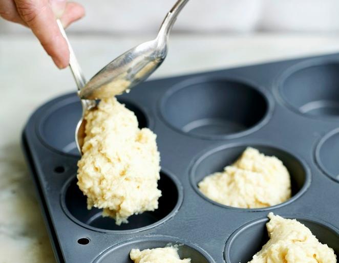 Klissete deig blir lagt i muffinsformer ved hjelp av skeier. Foto.