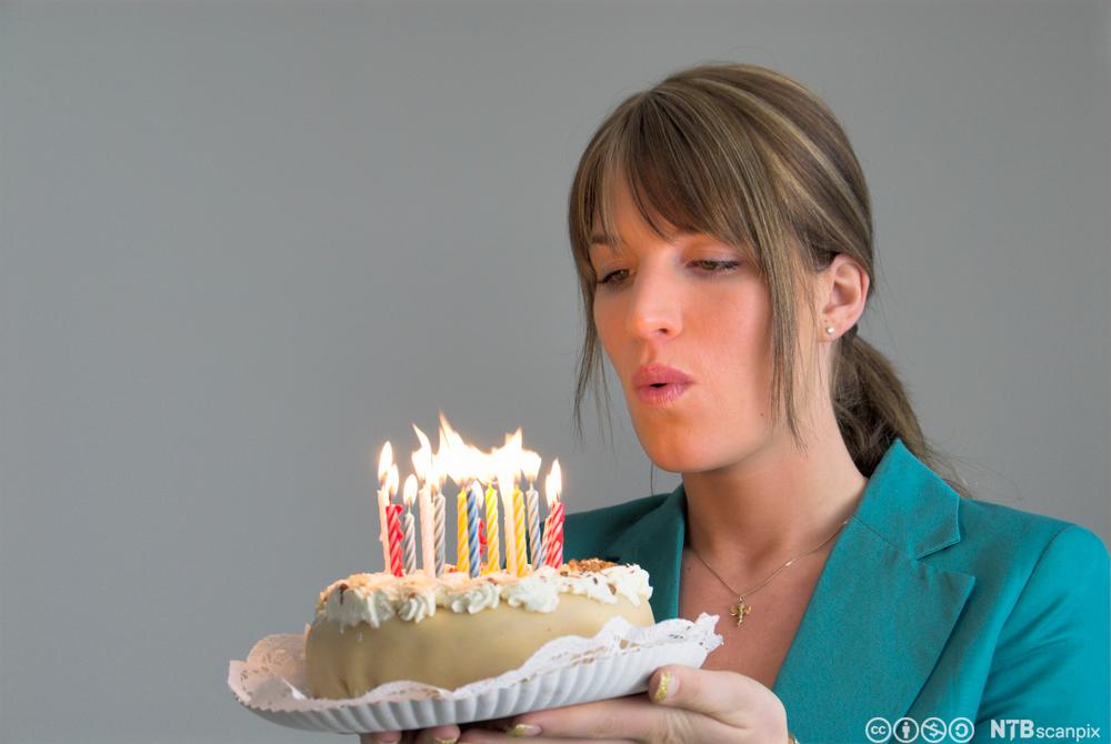 En dame som blåser lysene på bursdagskake. Bilde.