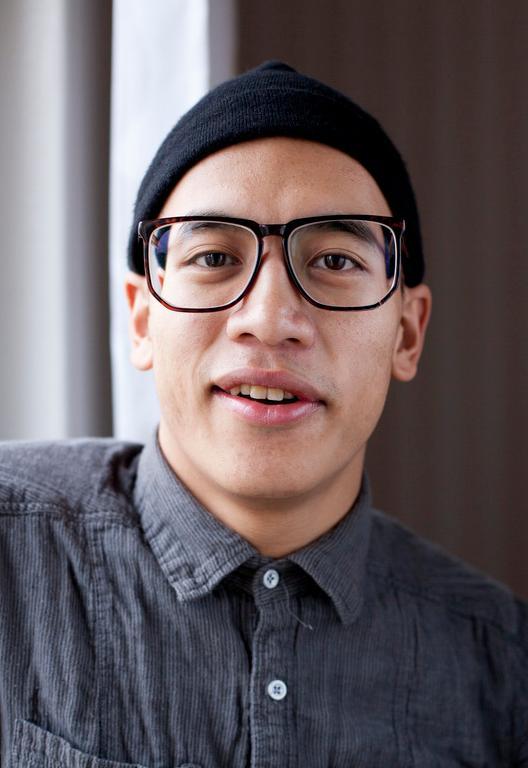 Portrett av ung mann med skjorte, briller og lue. Foto.