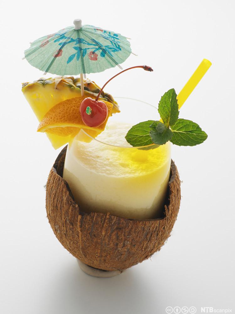 Eit glas med piña colada plassert i ei kokosnøtt. Foto.