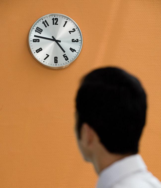 Ung mann ser på ei klokke på veggen. Foto.