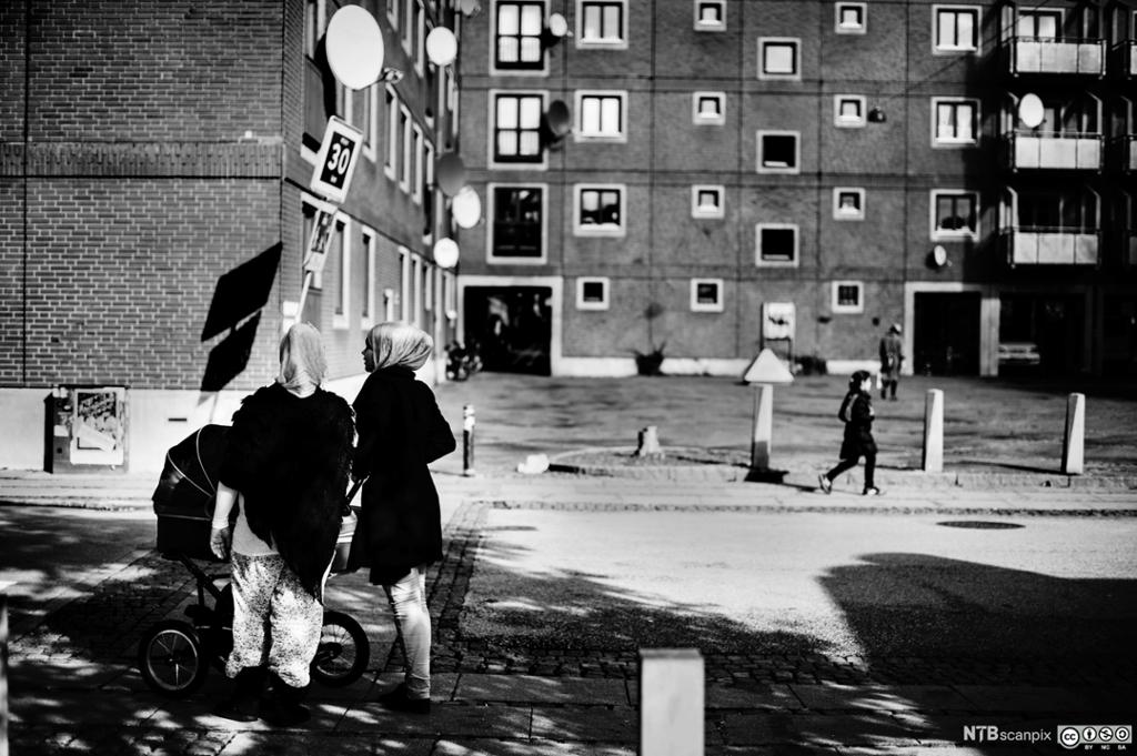 To muslimske kvinner med barnevogn står utenfor noen boligblokker. Foto.