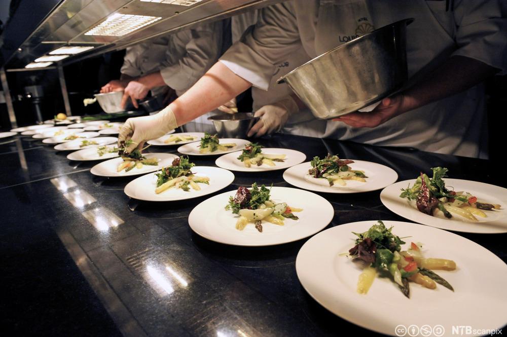 Kokker legger opp mat på mange tallerkener til et selskap. Foto.