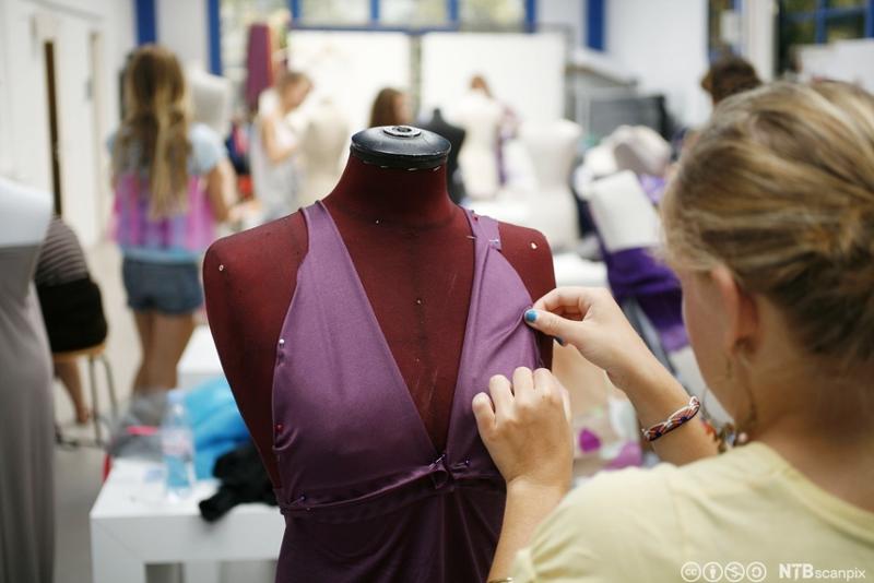 Klesdesigner som arbeider med en lilla kjole. Foto.