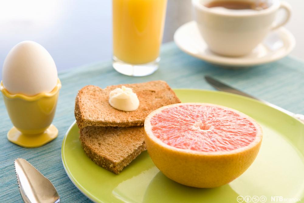 Frokost med grapefrukt, brød, egg, juice og kaffe. Foto.