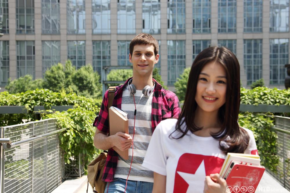 To studenter med bøker i hendene, en jente og en gutt, på campus. Bilde.