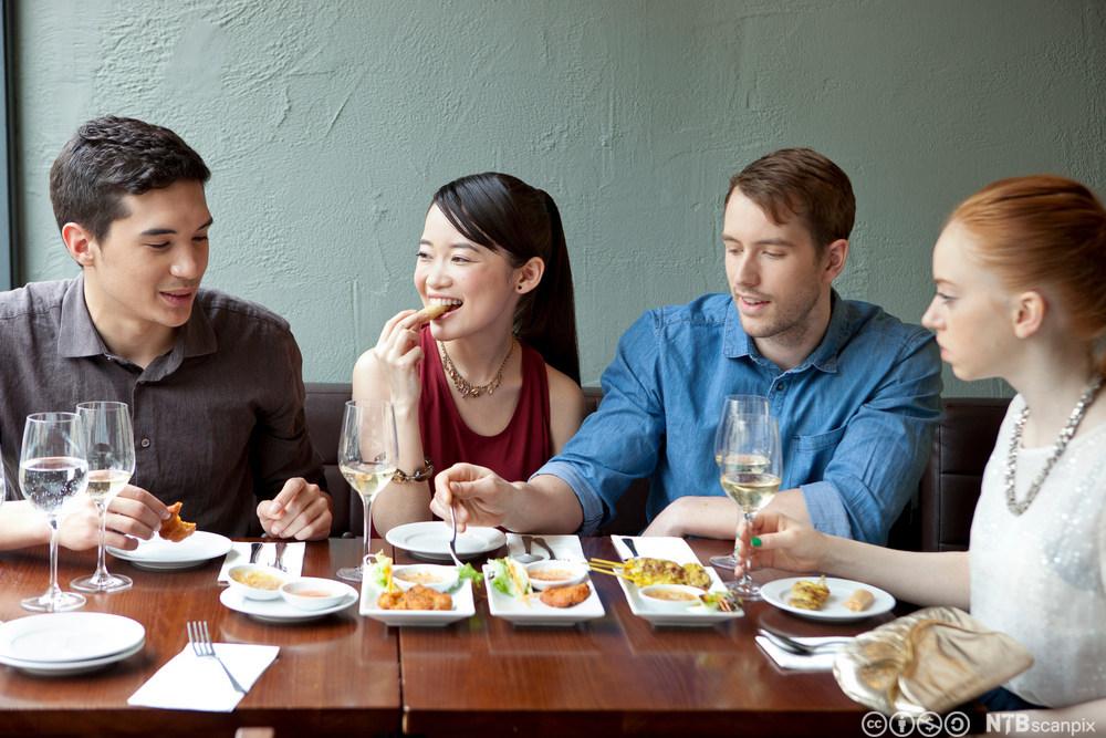 Fire unge mennesker spiser middag på restaurant. Foto.