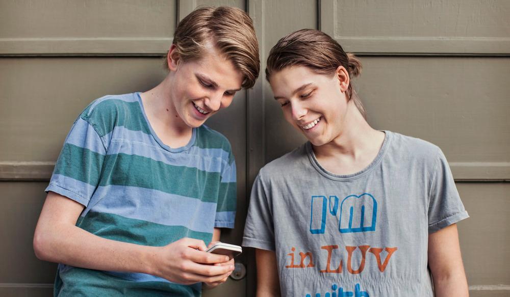 To gutar smiler mens dei ser på ein mobil. Foto.