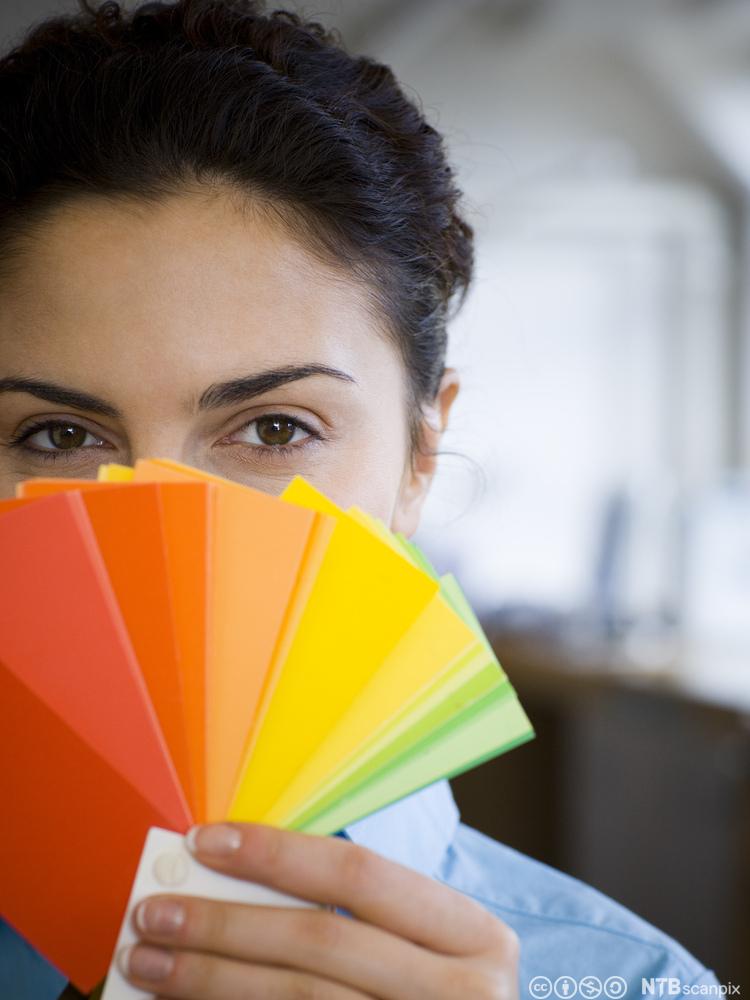 Kvinne med fargekart foran ansiktet. Foto