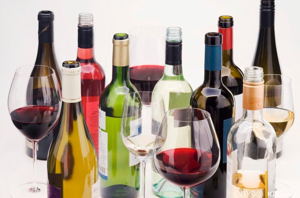 Vinflasker og glass med vin i mot hvit bakgrunn. Foto.