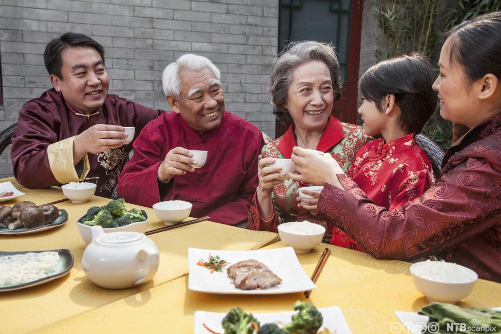 Tre generasjoner kinesere skåler med kopper på en restaurant. Foto.
