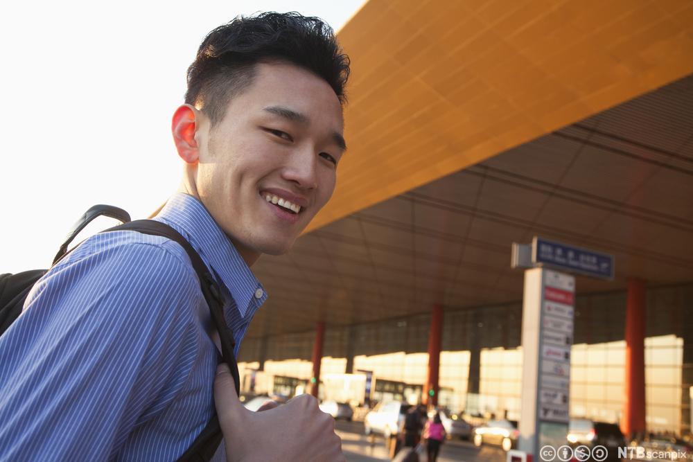 Ung kinesisk mann på vei inn på en flyplass. Foto.
