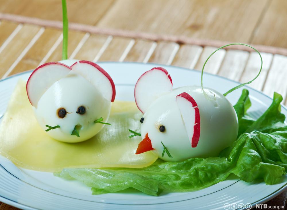 To egg som er dekorerte med peparkorn og diverse grønsaker slik at dei ser ut som mus. To reddikskiver som er stukne inn i kvart egg, tener som øyre. Foto.