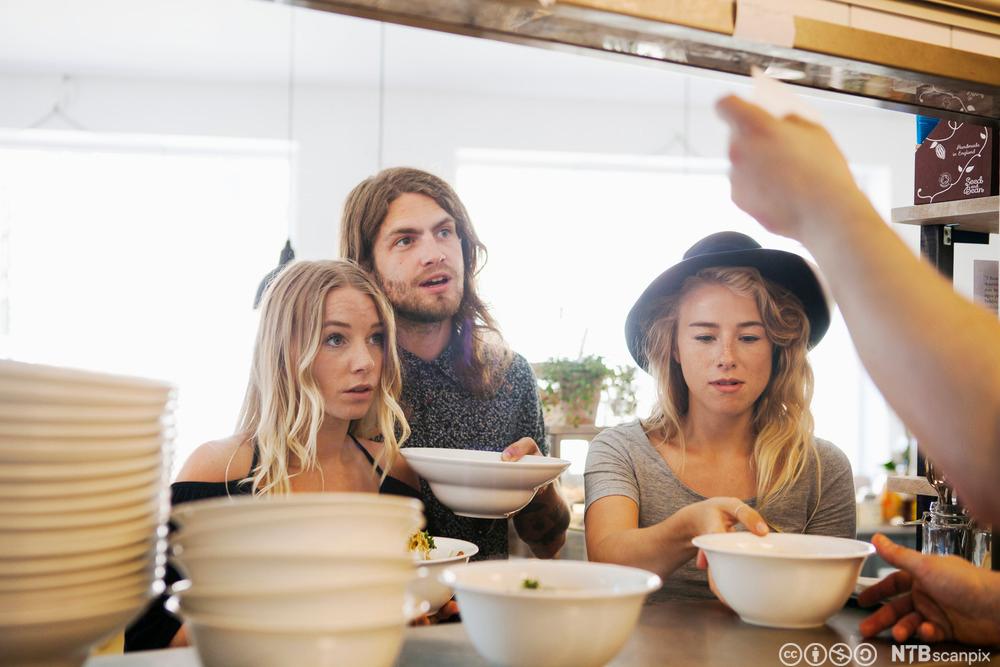 Tre unge mennesker som bestiller mat over en disk. Foto.