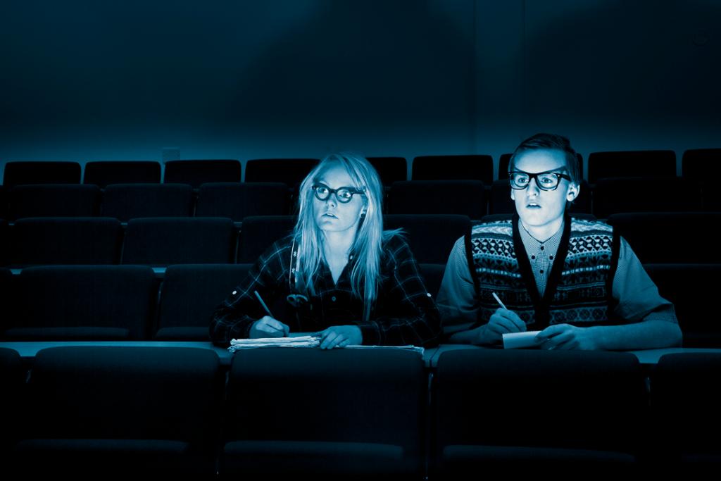  To ungdommer med penn og papir foran en skjerm, klare til å anmelde en film. Foto.