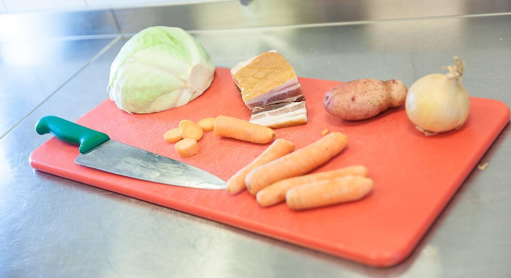 Kokkekniv, rå grønnsaker og bacon på en skjærefjøl. Foto.