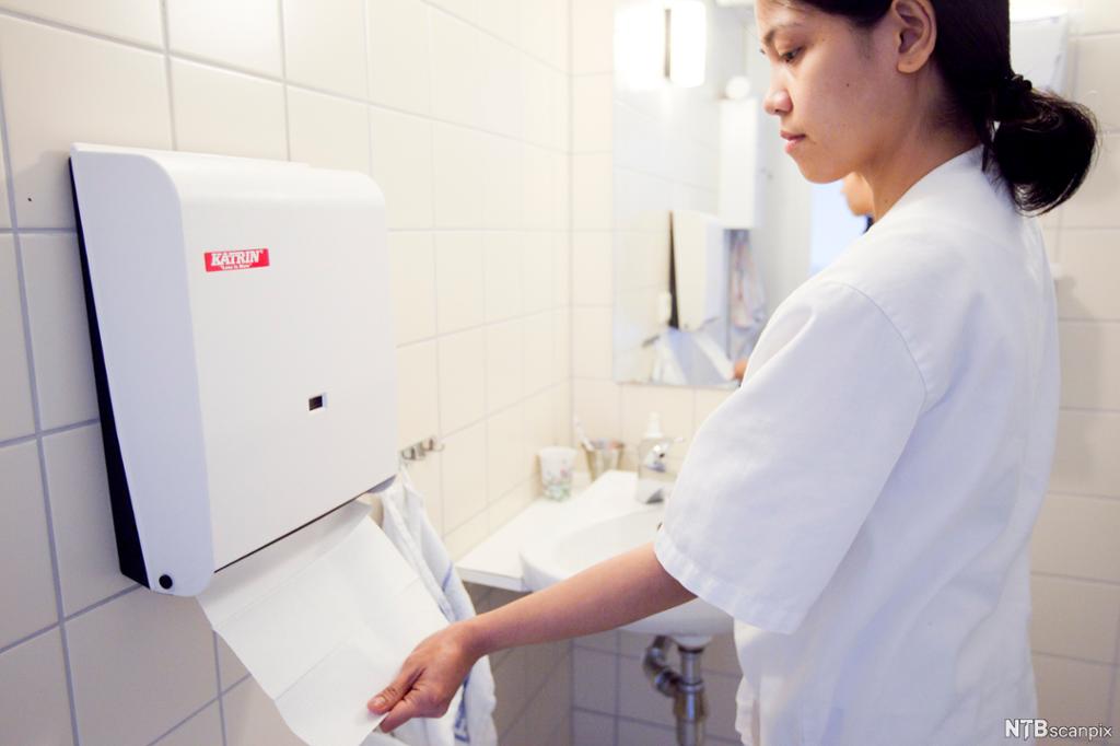 Helsefagarbeidar tørkar hendene med papir etter handvask. Foto.